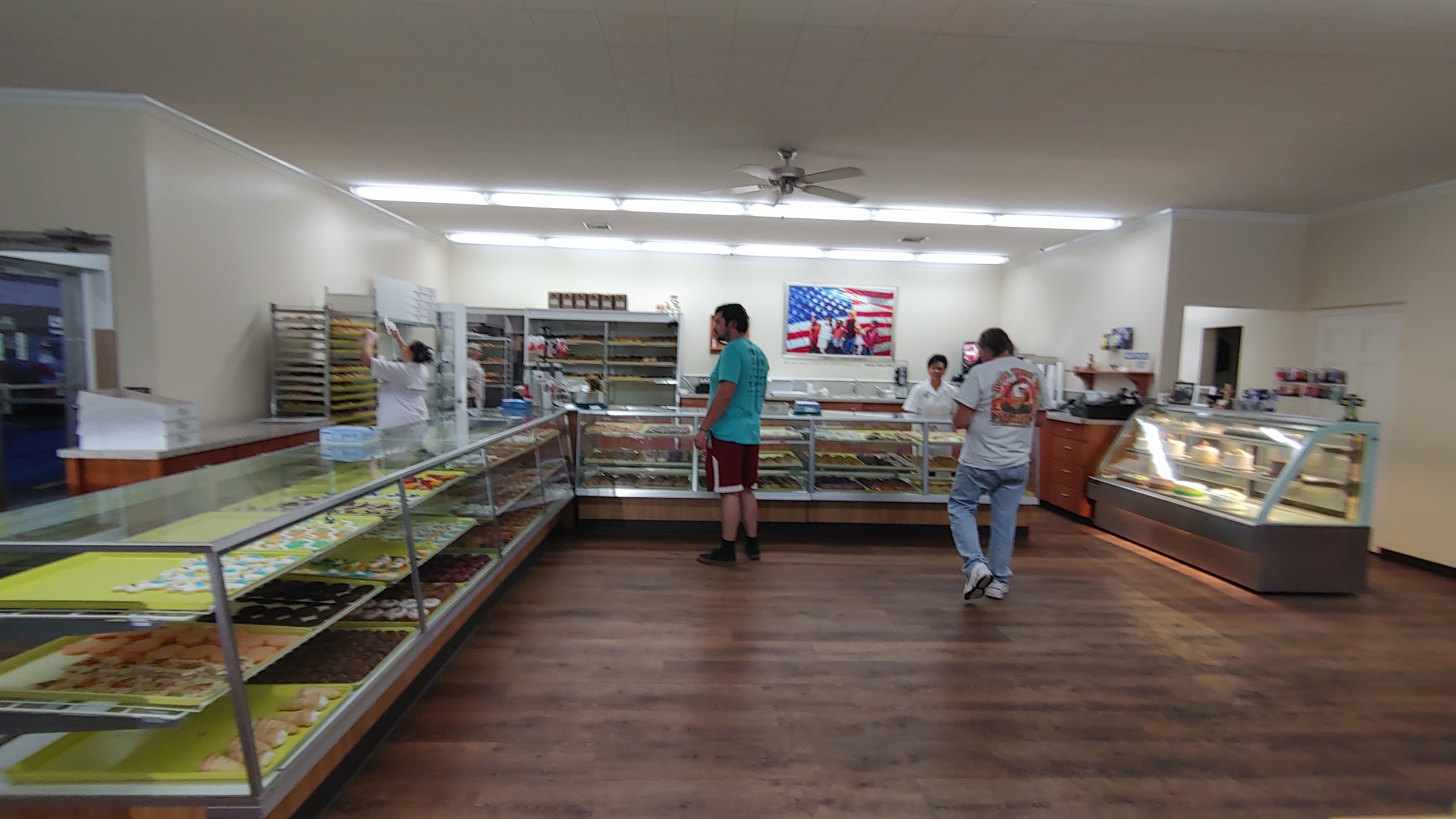 Inside Marge's Donut Den — long glass display cases, staff working, customers, and American-flag wall art